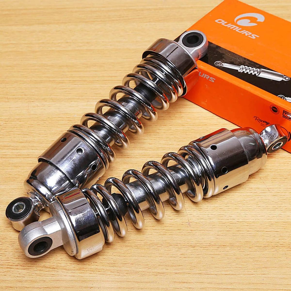 Pair of chrome rear shocks with black coil springs and top mounting eye, angled view.