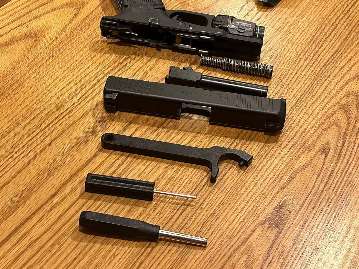 Disassembled black pistol parts on wood with included black tools and pins