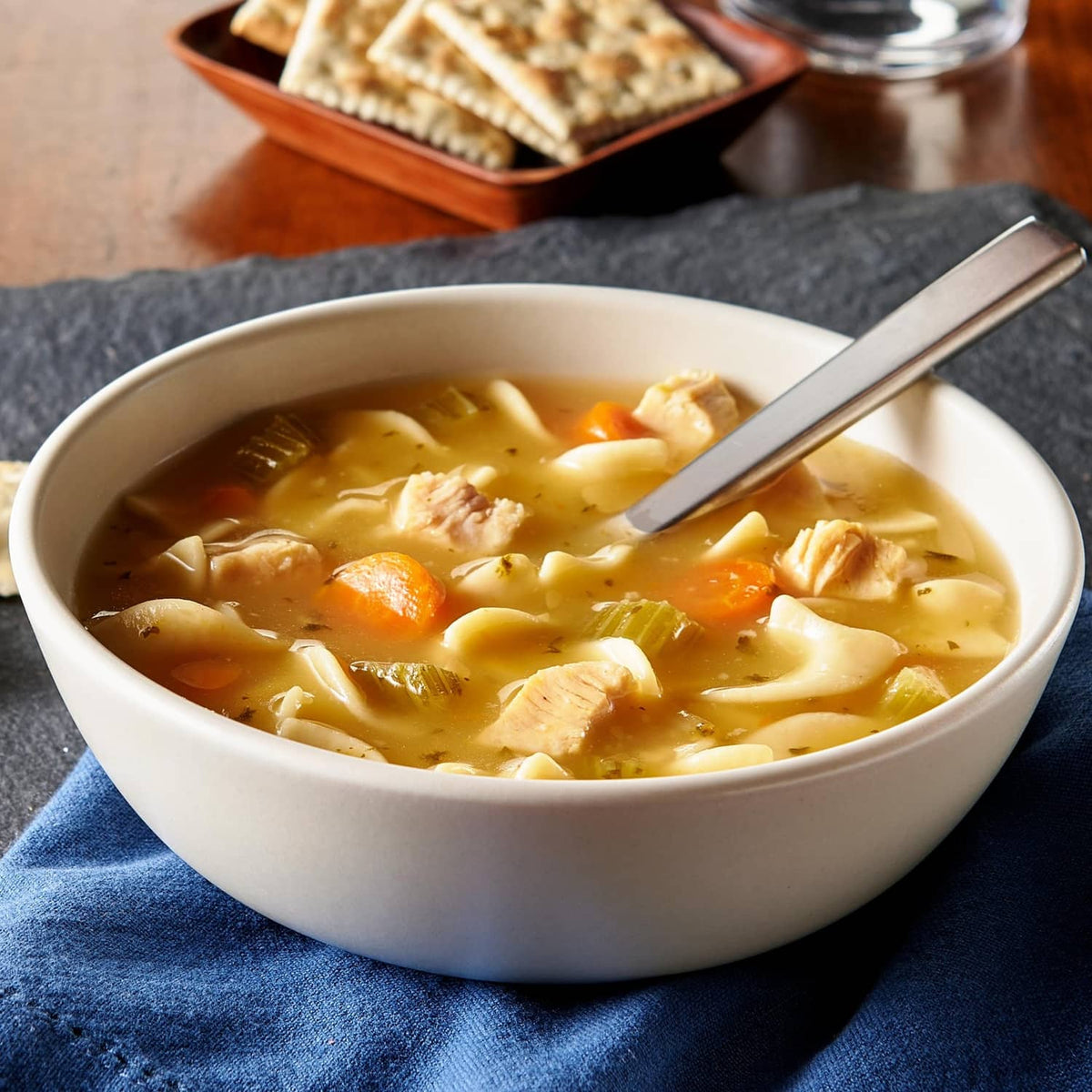 Chicken noodle soup in white bowl with spoon, carrots, and chicken pieces