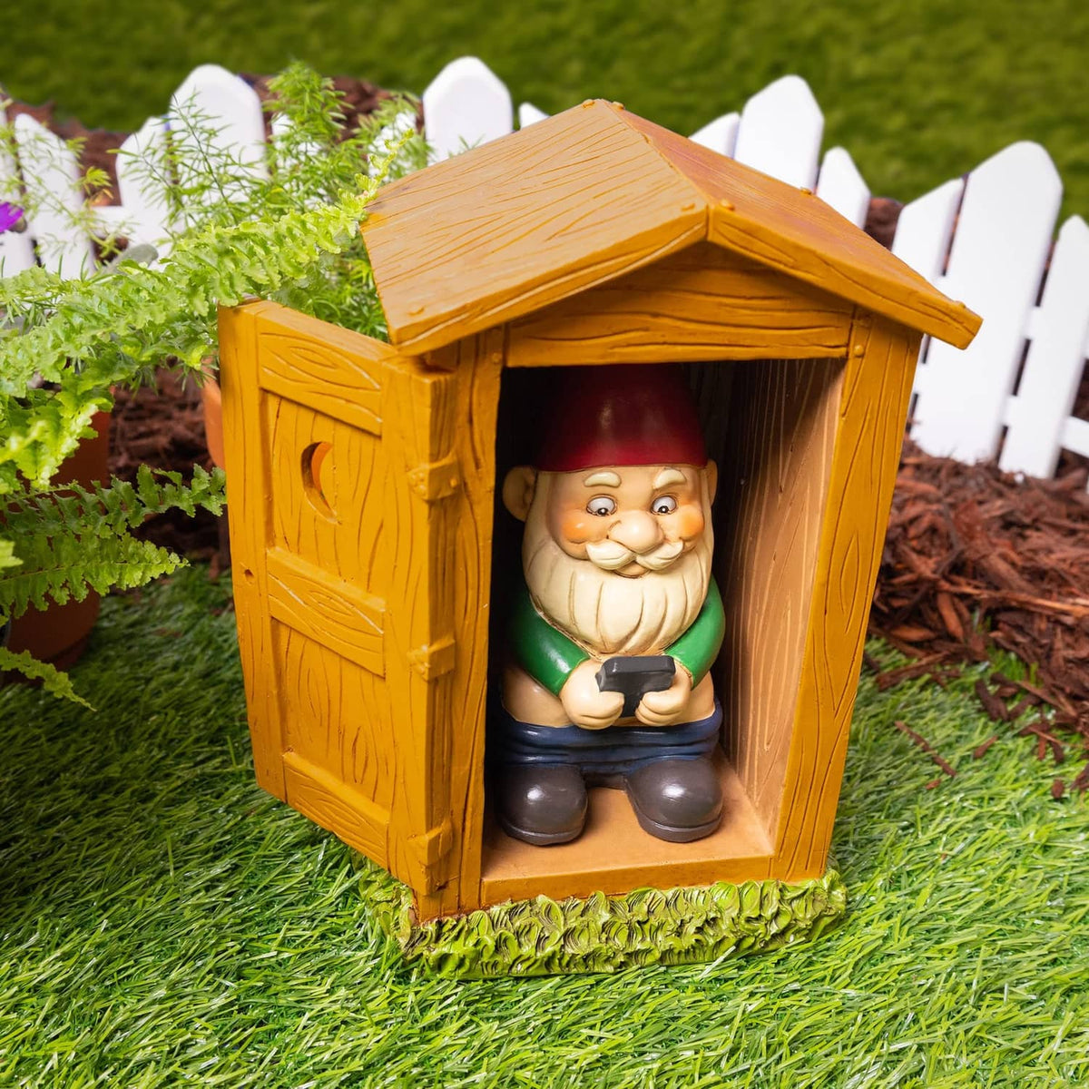 Garden toilet gnome statue in wooden outhouse with red hat, on green turf base