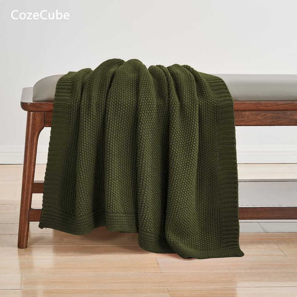 Olive green knit throw blanket draped over a wooden bench, lounge style.