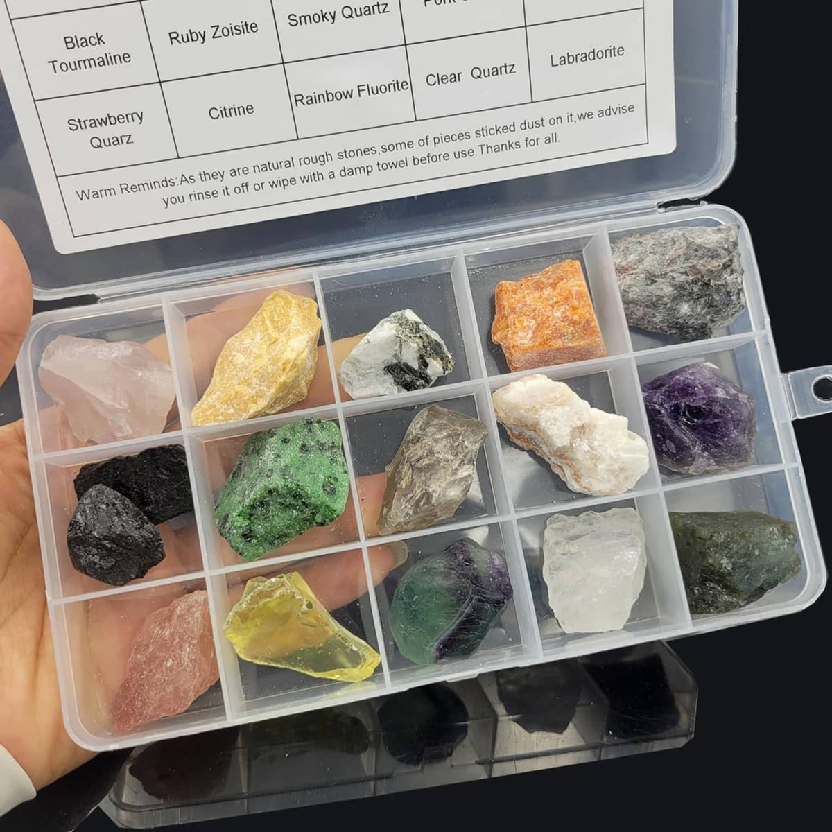 Rock tumbling rough stone specimen kit in clear organizer box, hand holding the tray