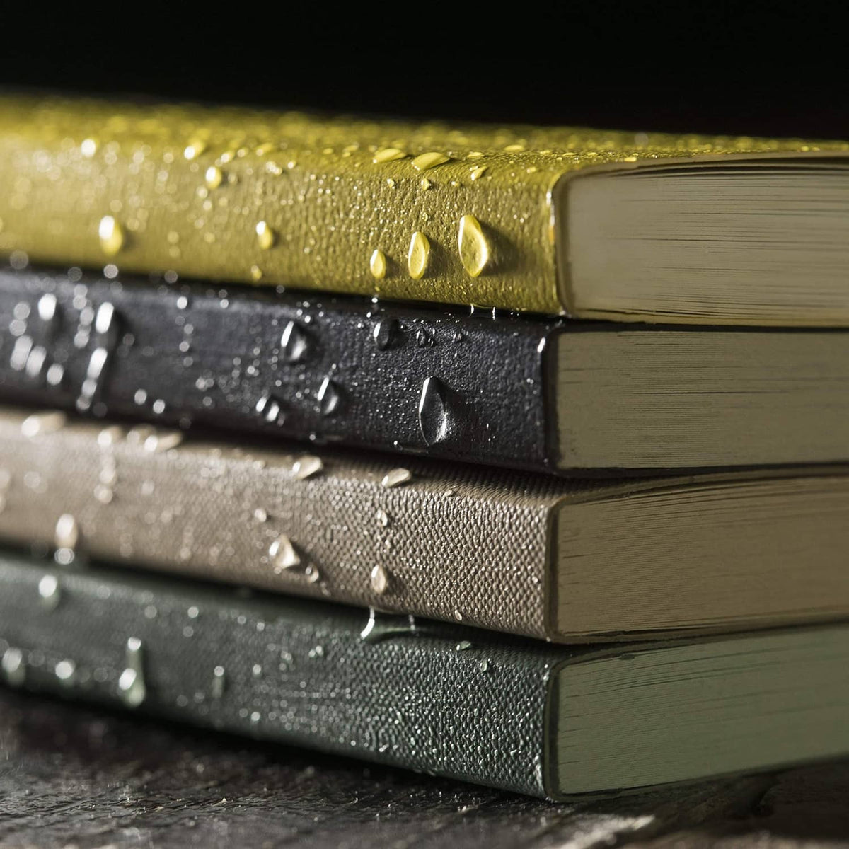 Weatherproof pocket notebooks stacked, textured covers with water droplets and close-up of spines