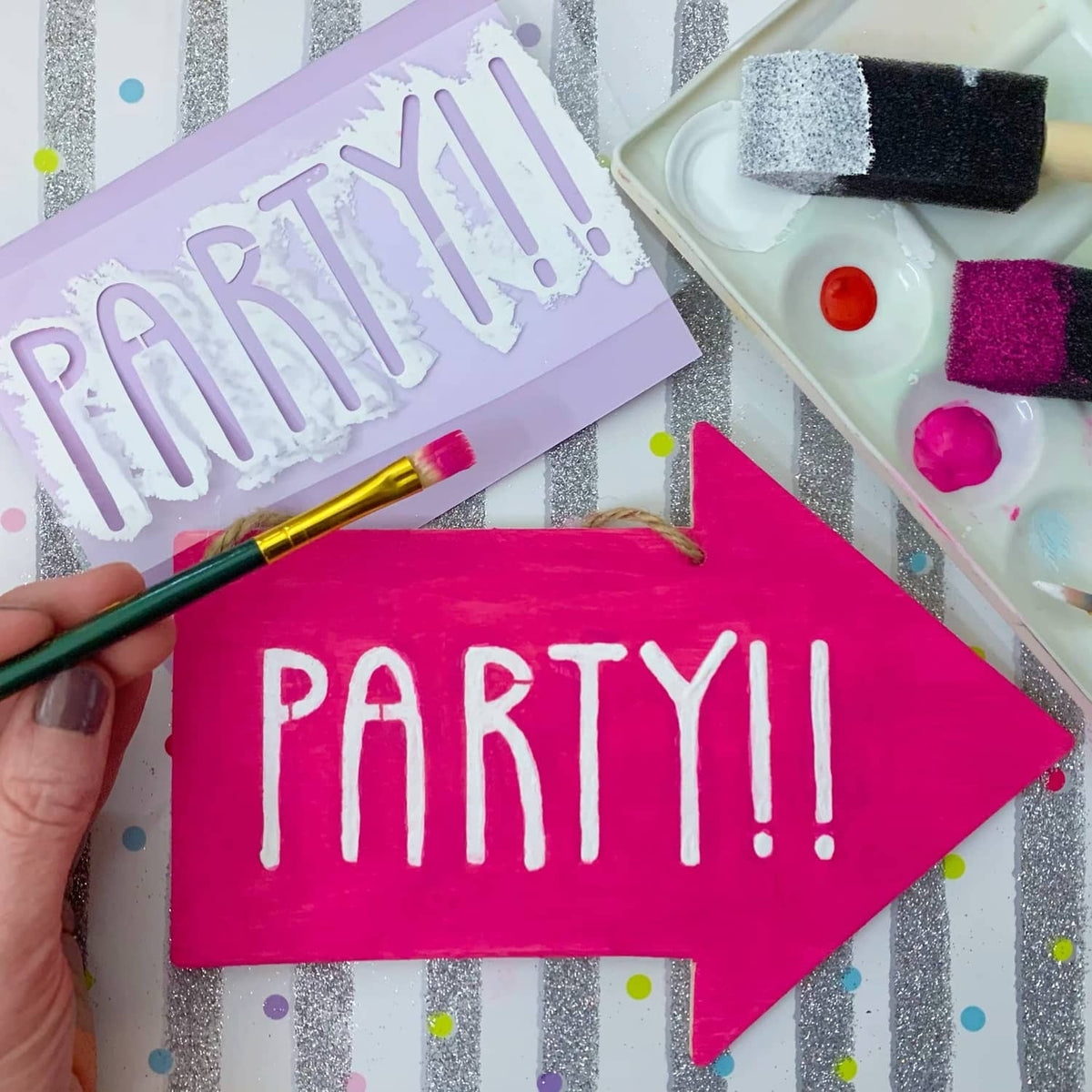 Pink arrow stencil with PARTY!! text, paintbrushes and foam tools