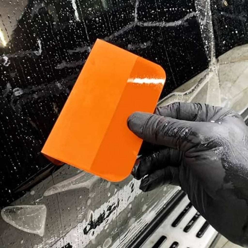 Orange TPU squeegee with gloved hand on glass panel to remove water or film