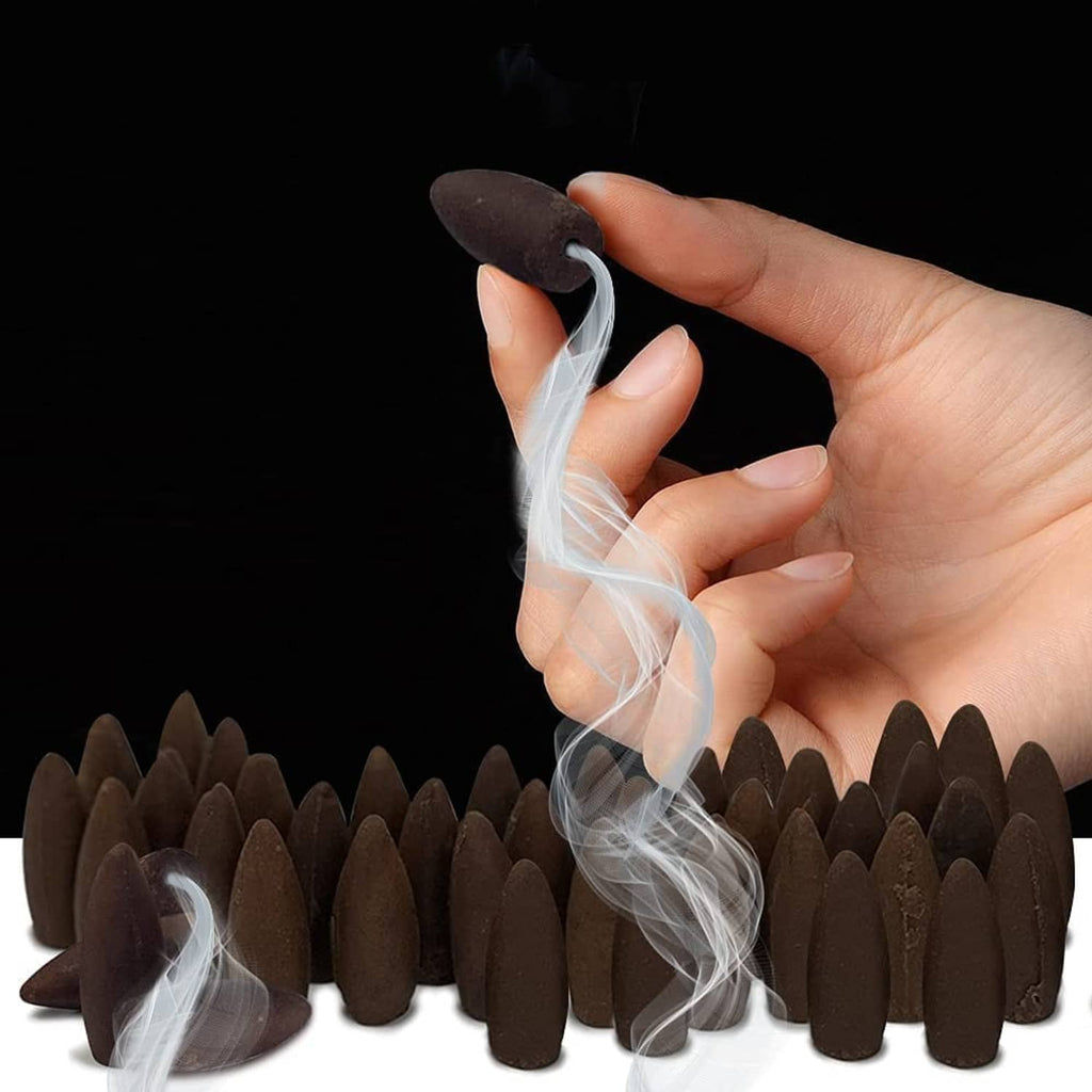 Hand holding a dark brown backflow incense cone with smoke rising over cones