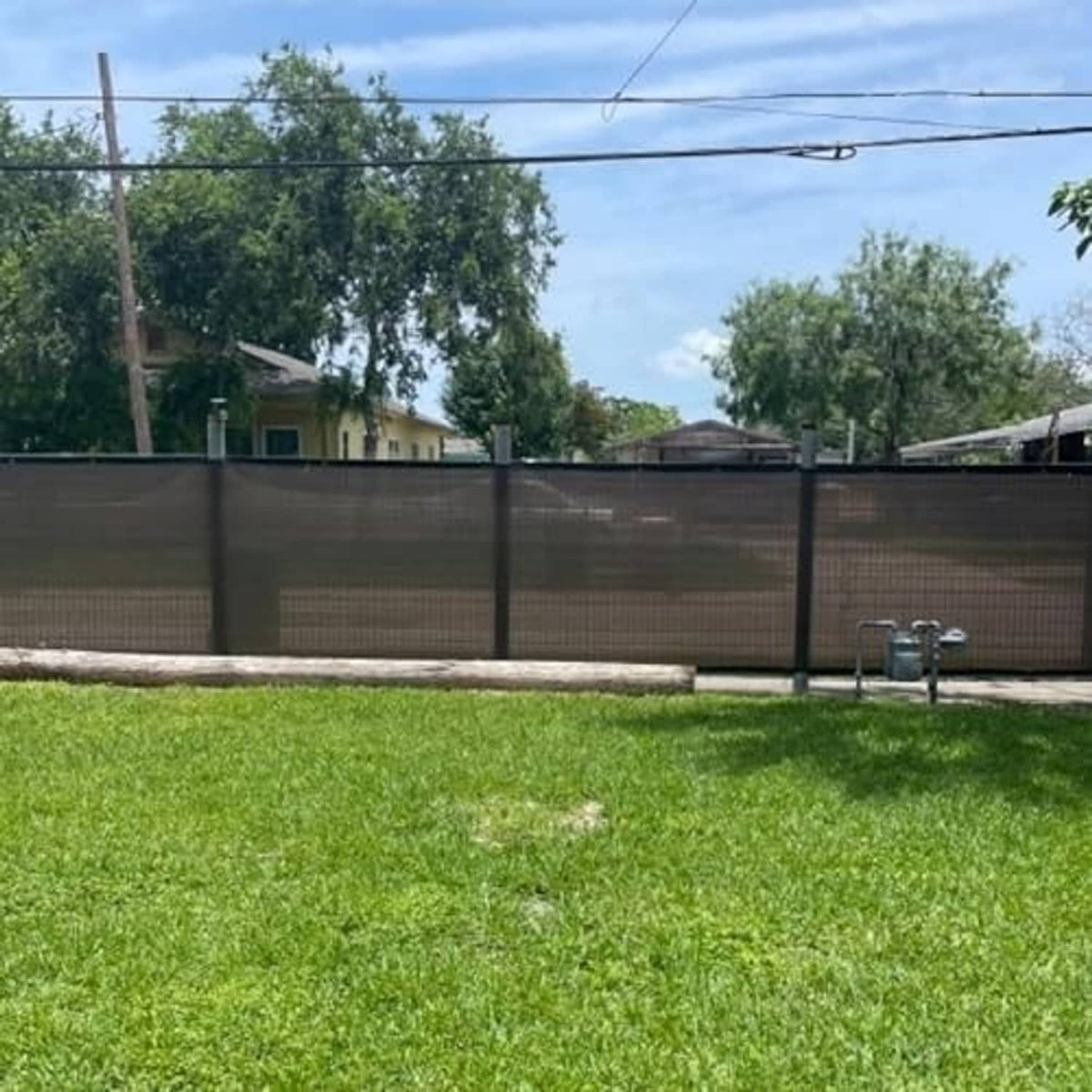 Brown woven privacy screen fabric installed along a backyard fence line