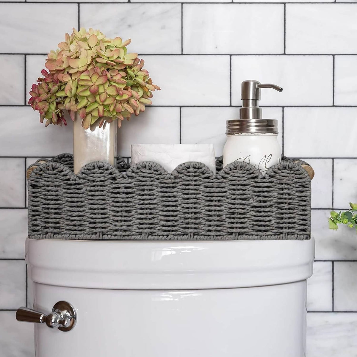 Grey wicker-style toilet paper storage basket with scalloped edge and wood handle tabs.