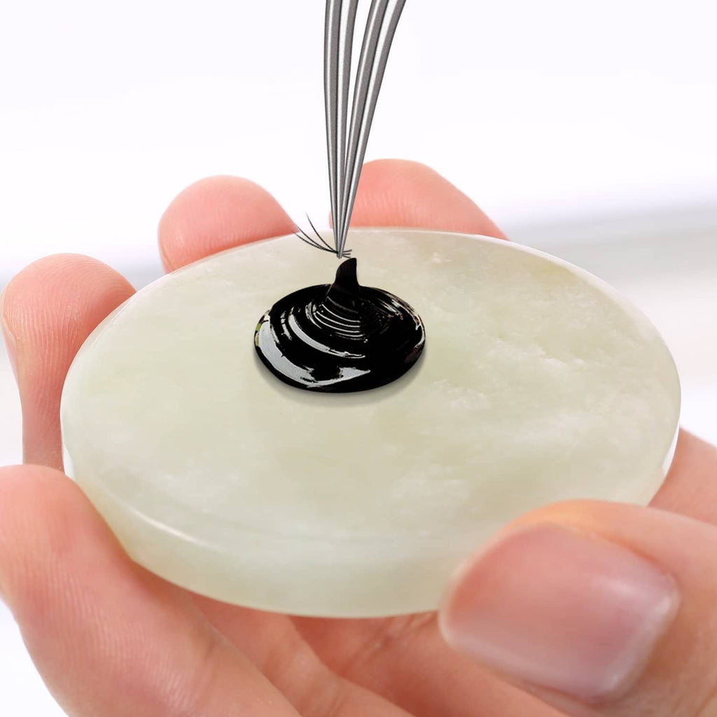 Round jade eyelash glue pad with a drop of black adhesive on top