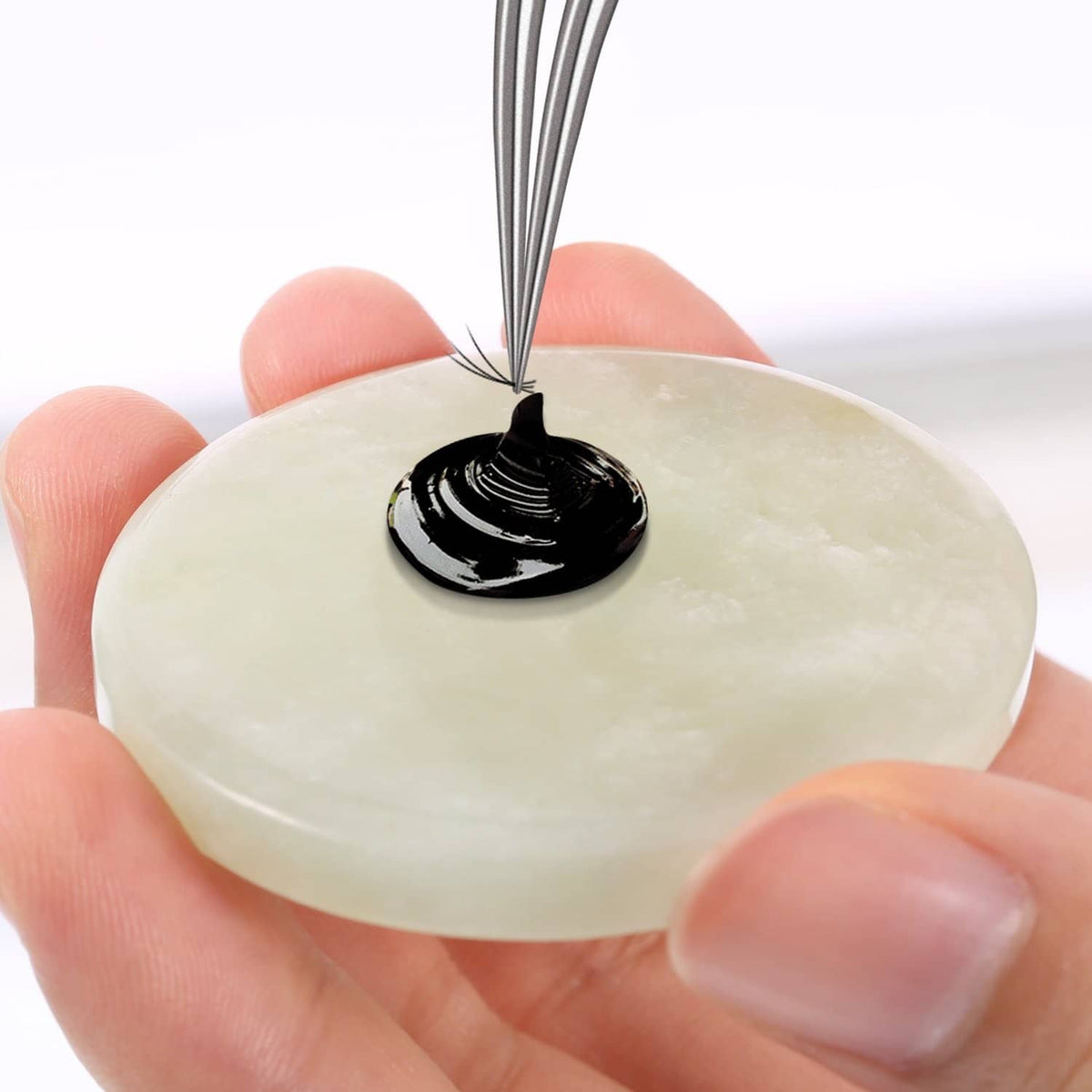 Round jade eyelash glue pad with a drop of black adhesive on top