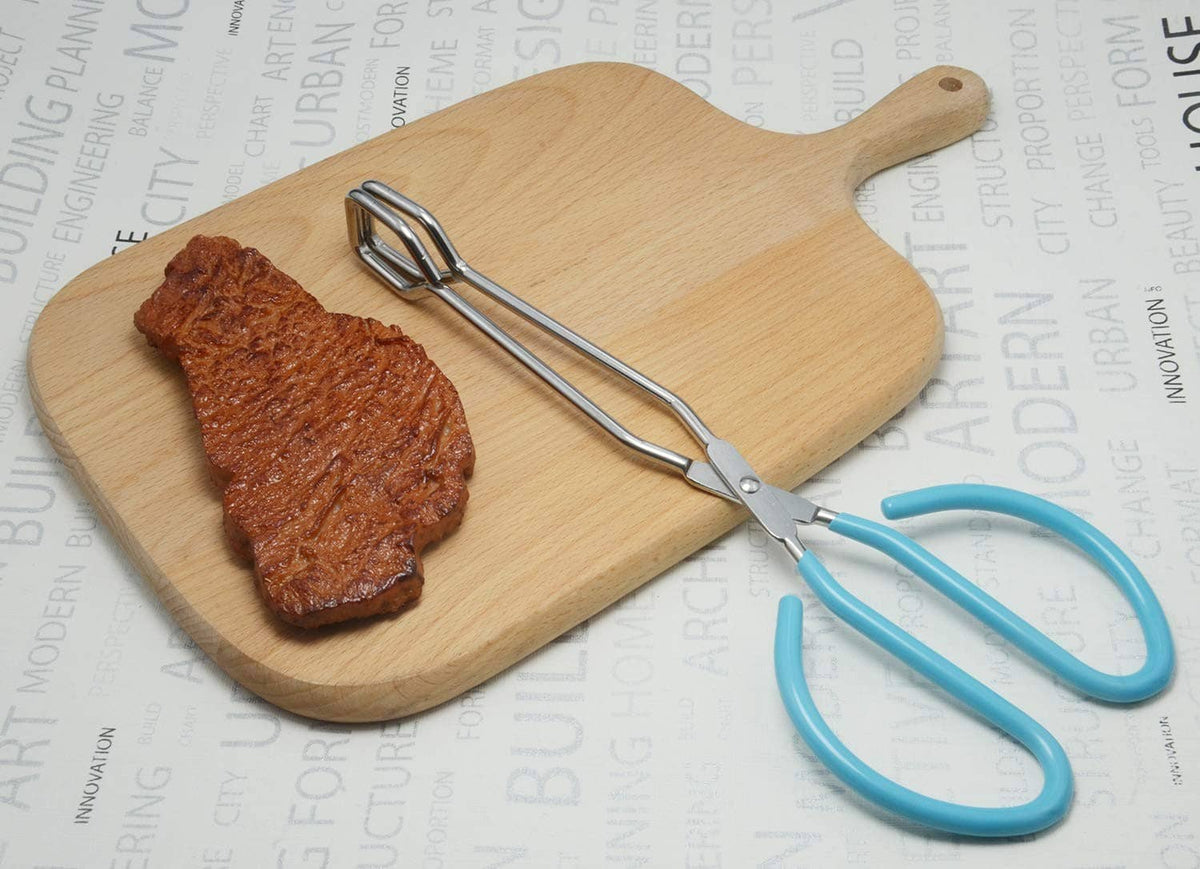 Stainless scissor tongs with teal handles on a wooden cutting board