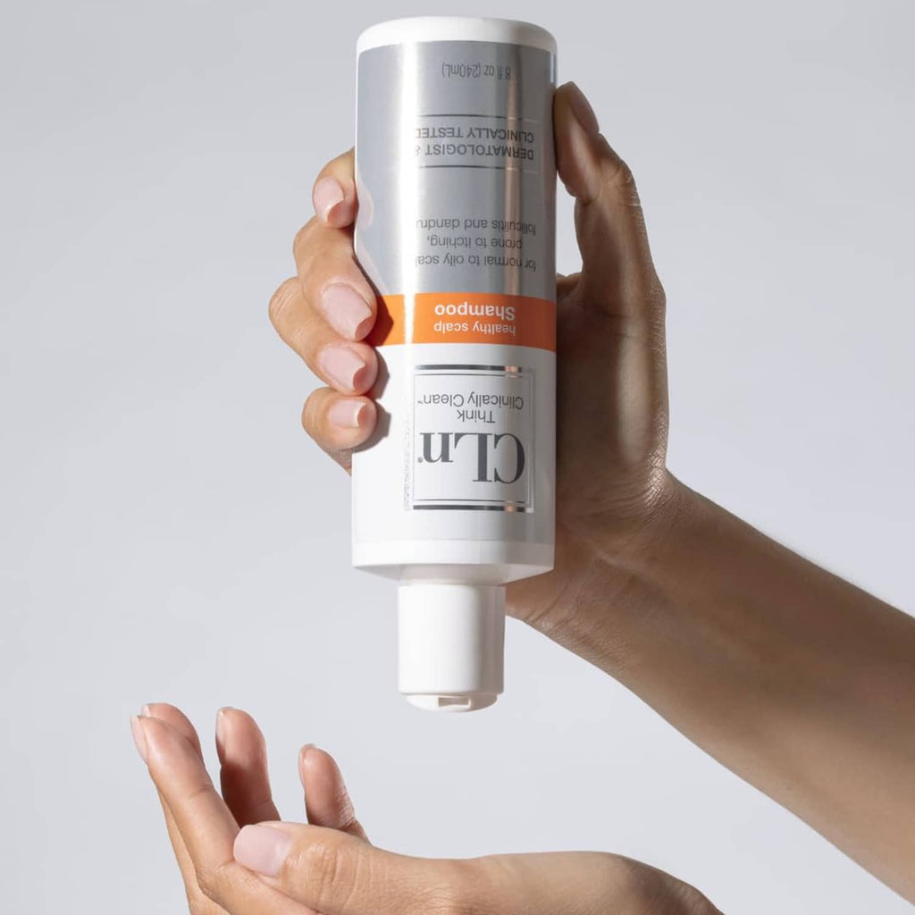Hand holding CLn healthy scalp shampoo bottle with white cap and orange label