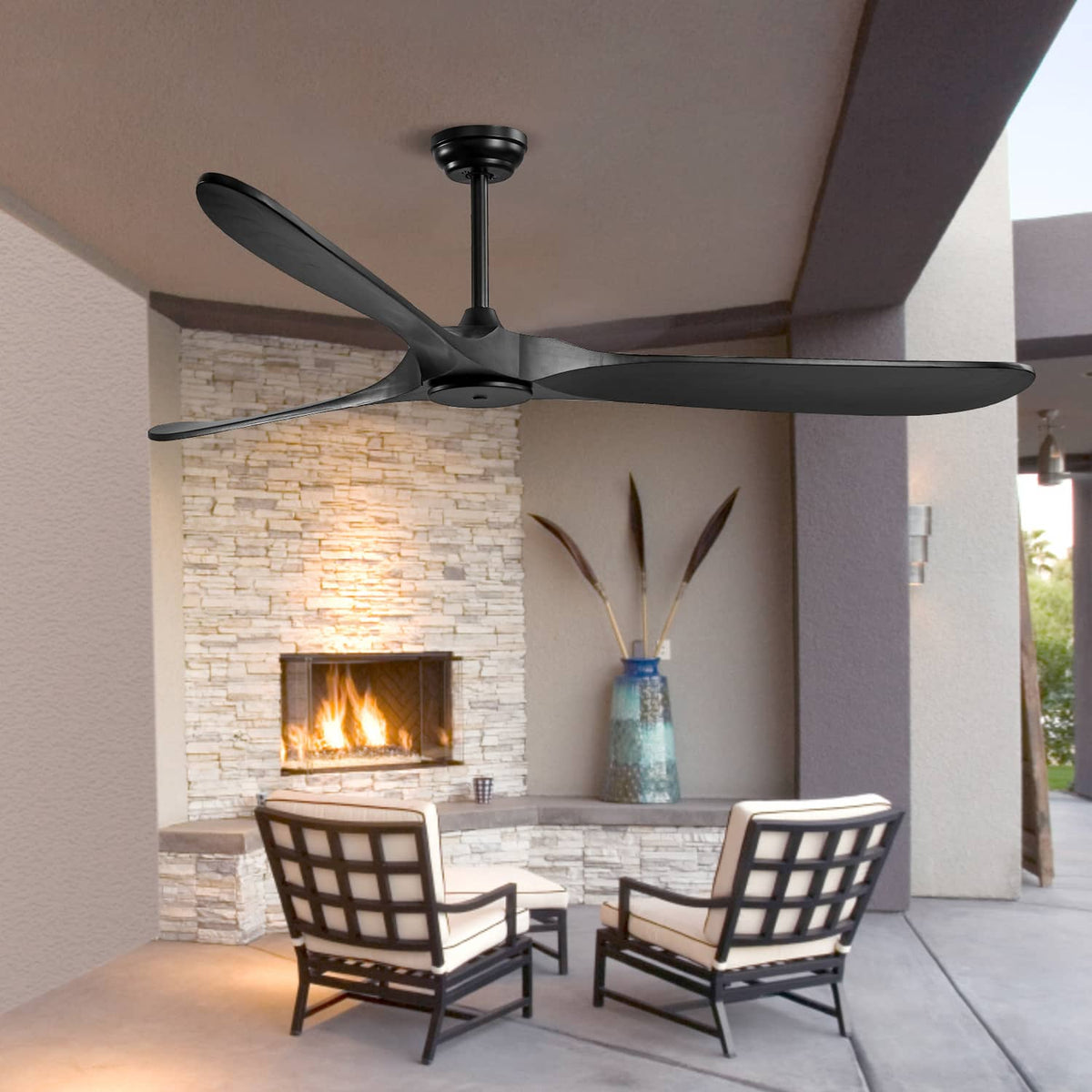 Black 3-blade ceiling fan installed on a covered patio with stone fireplace