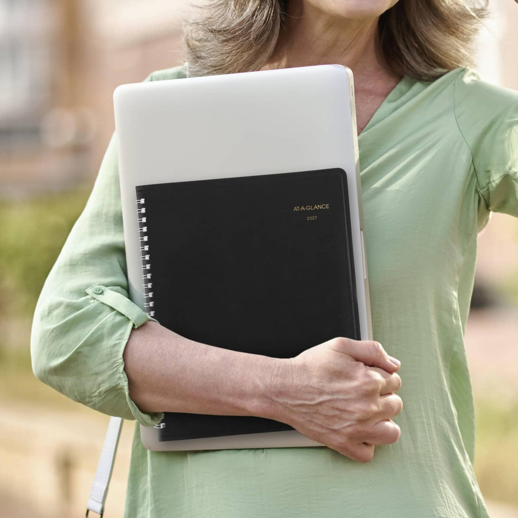 Black 2027 monthly planner held in hand with AT-A-GLANCE logo on cover