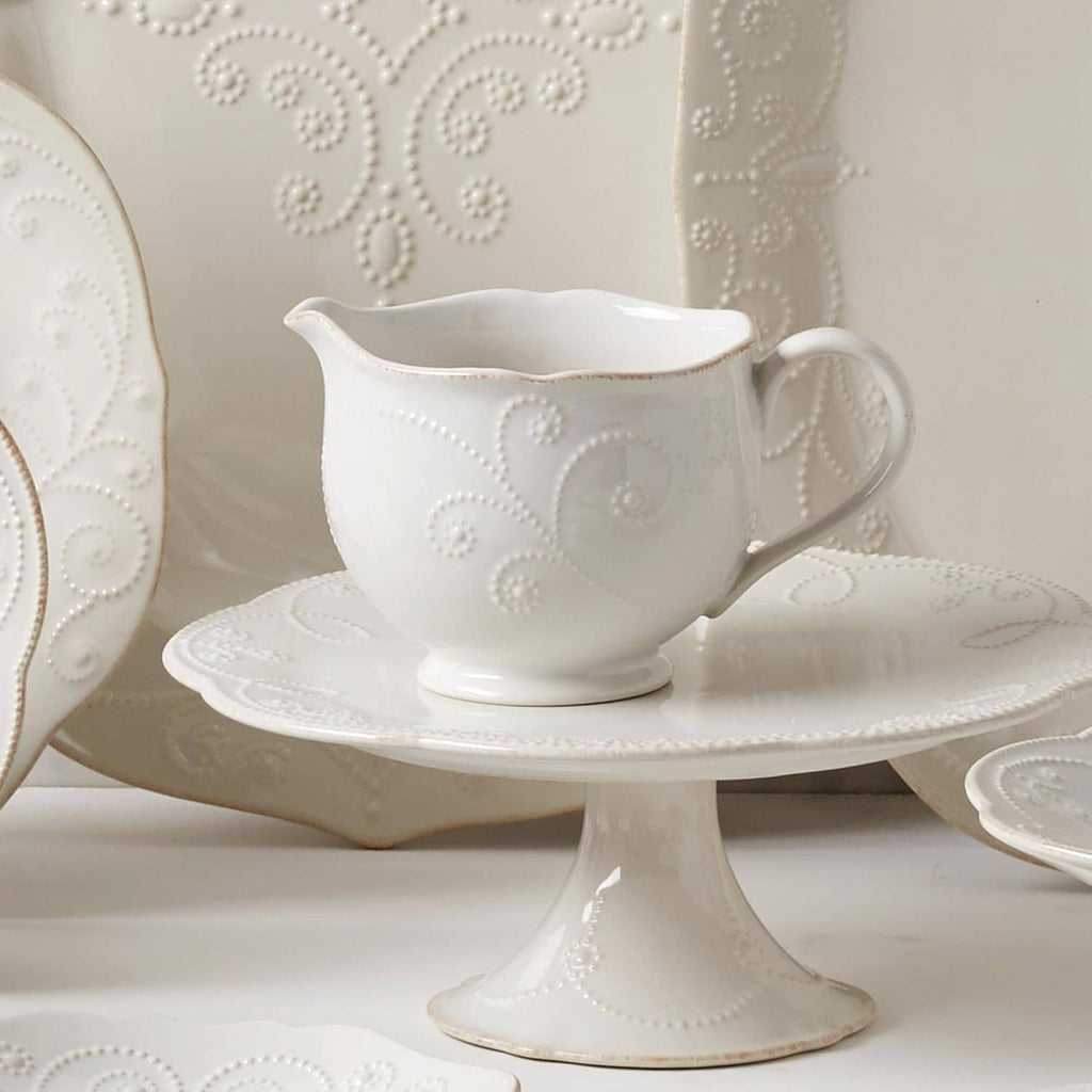 White ceramic sauce pitcher on matching pedestal saucer, embossed dot-and-vine motif