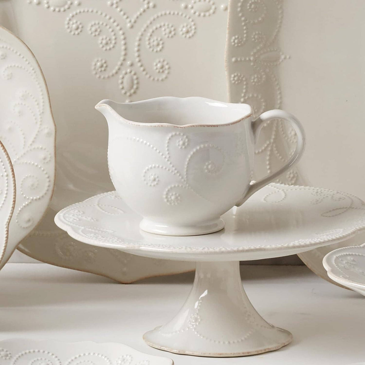 White ceramic sauce pitcher on matching pedestal saucer, embossed dot-and-vine motif