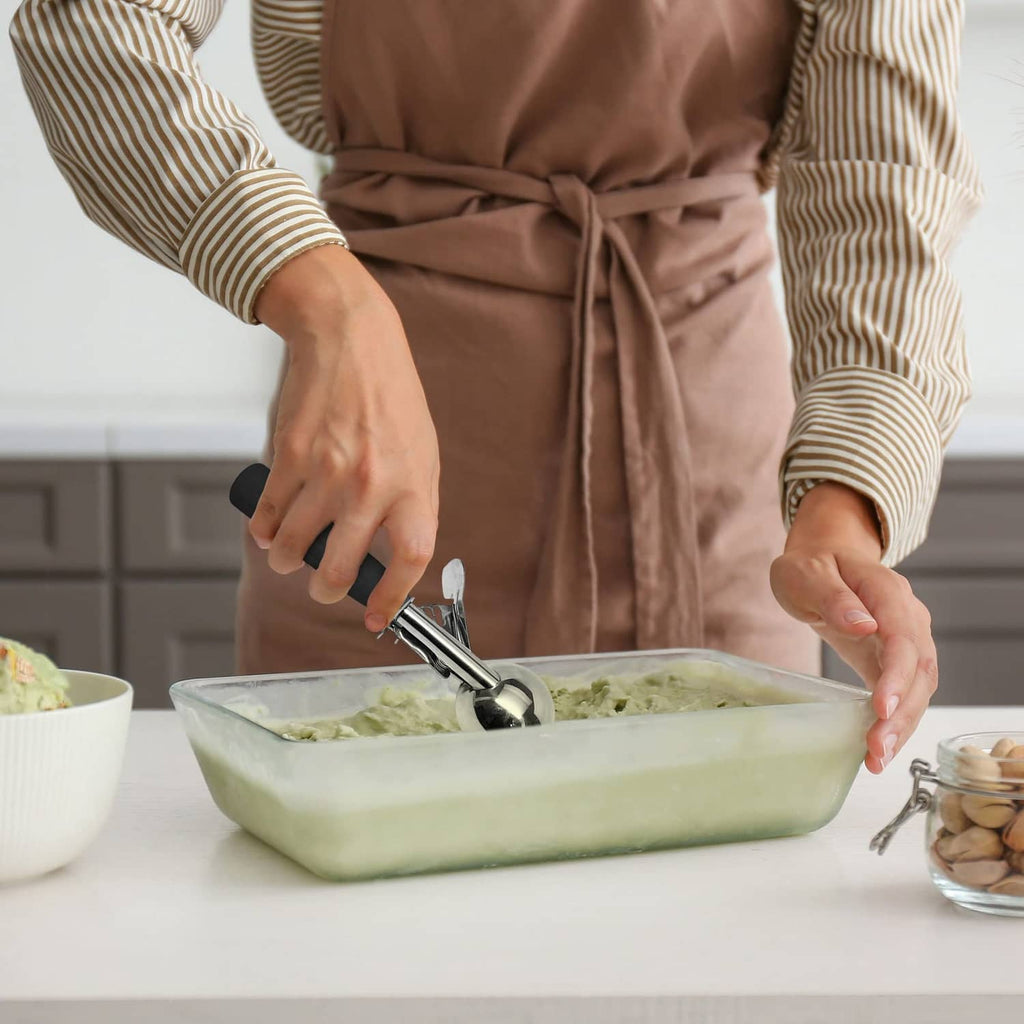 Black trigger scoop being used by hands to portion food from a glass container