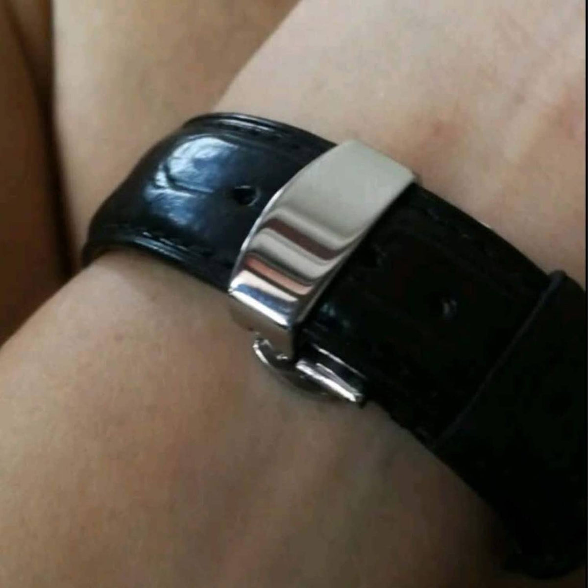 Silver deployant clasp on black leather watch strap, worn on wrist