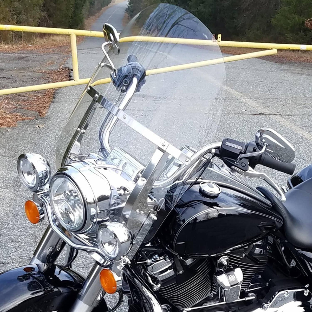 Clear motorcycle windshield with metal support brackets and quick-release hardware on bike