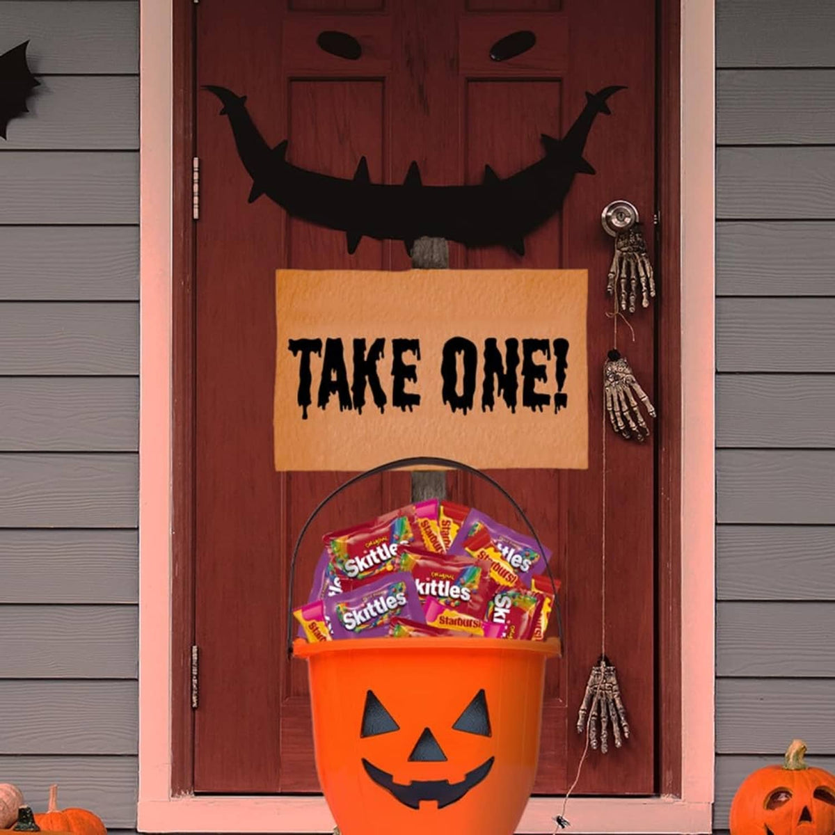 Halloween doorway candy basket with orange jack-o'-lantern bucket holding Skittles bags