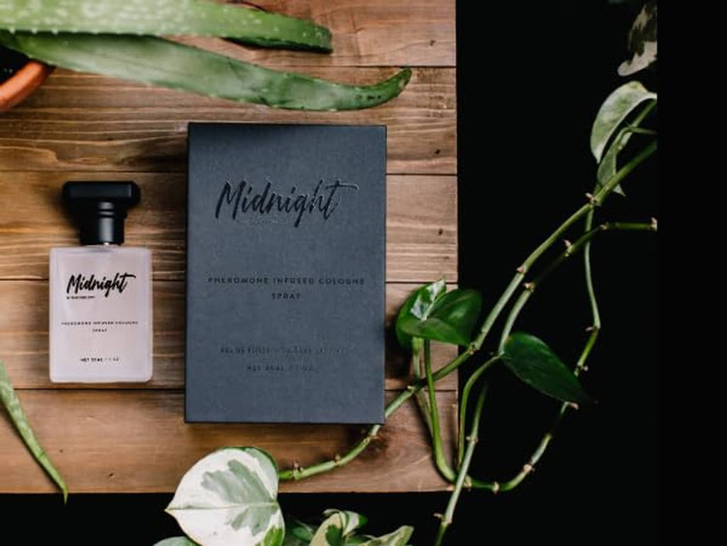Cologne spray bottle with gift box and foliage on wooden surface