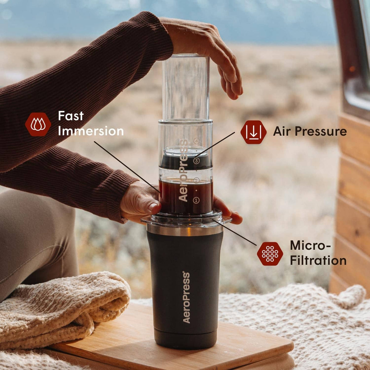 Portable AeroPress coffee maker with clear chamber on black base during brewing.