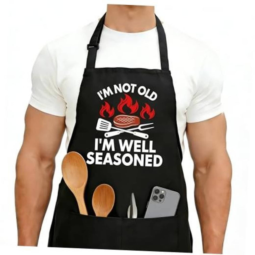 Black apron worn over a white shirt, front print with flames, grill, and utensils quote