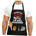 Black apron worn over a white shirt, front print with flames, grill, and utensils quote