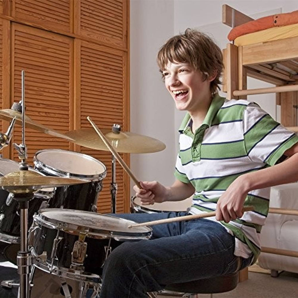Child holding maple wood drumsticks and playing a drum set