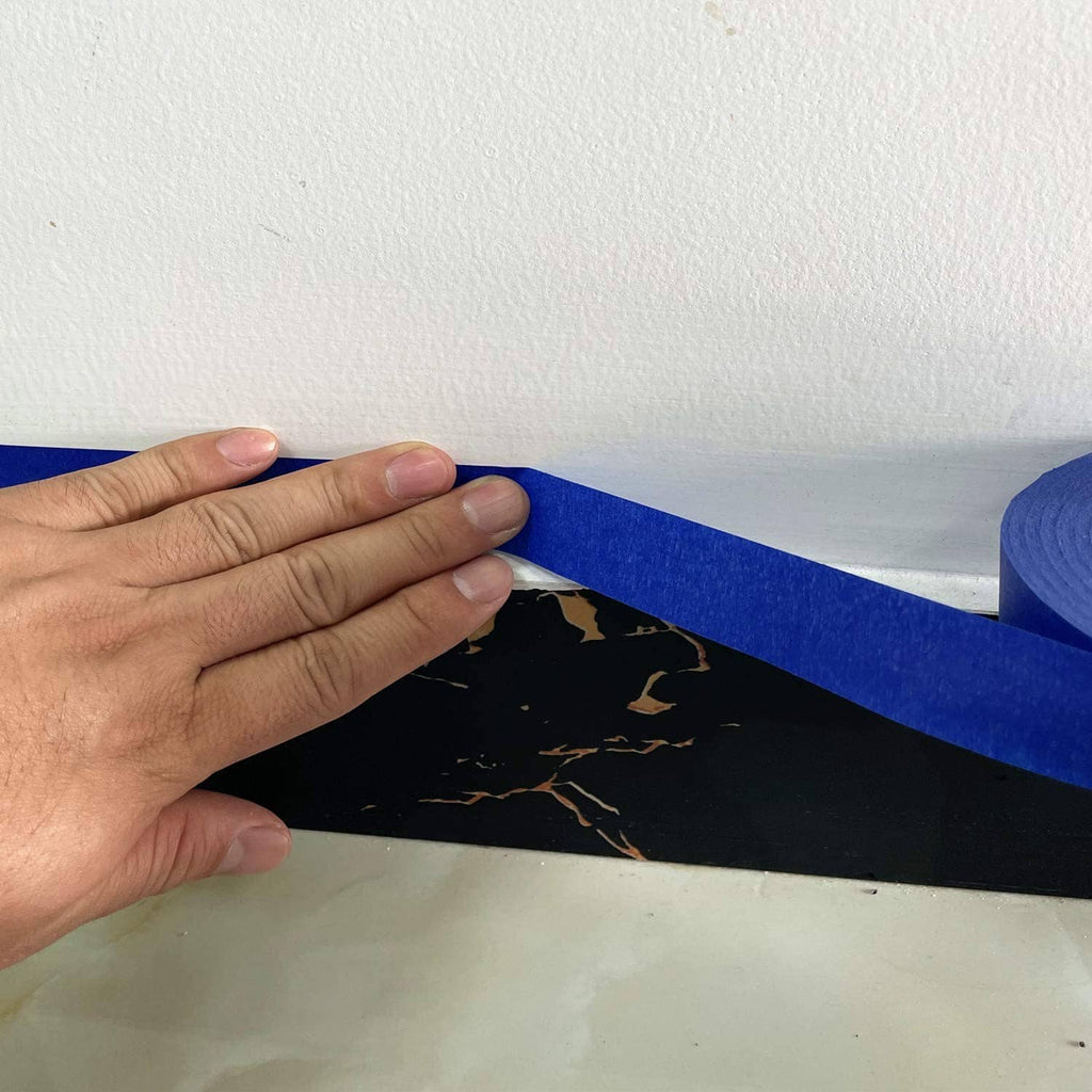 Hand smoothing blue painter’s tape strip onto a surface.