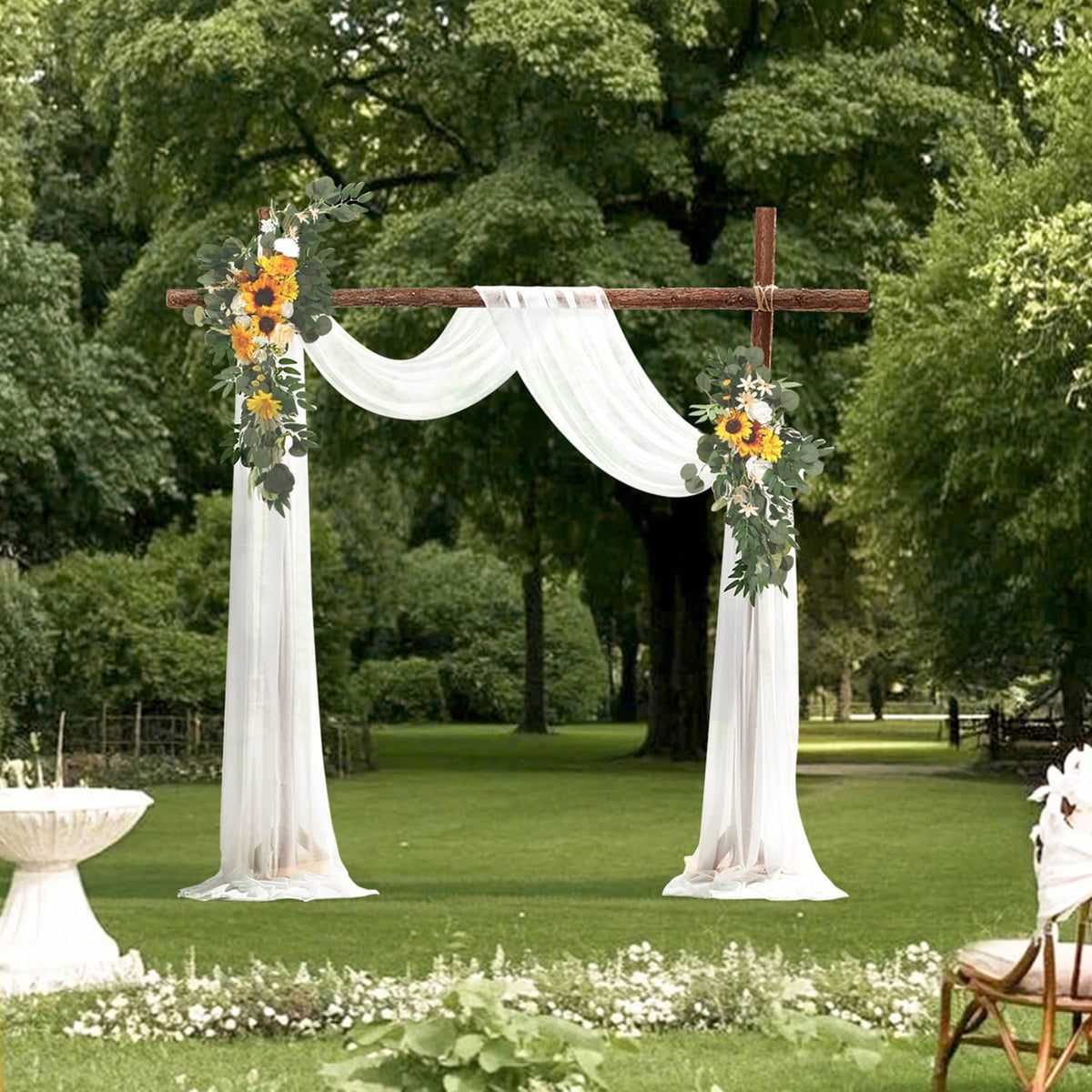 Outdoor wedding arch floral kit with white sheer drapes and yellow-orange faux flowers on greenery