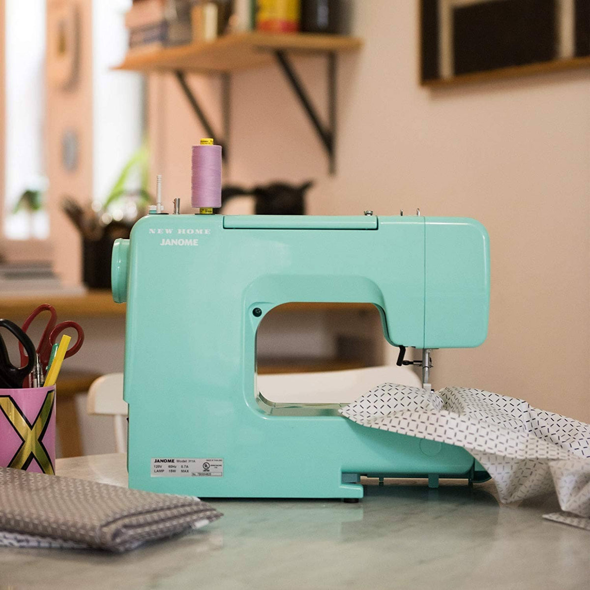 Turquoise sewing machine with presser foot over patterned fabric and thread spool