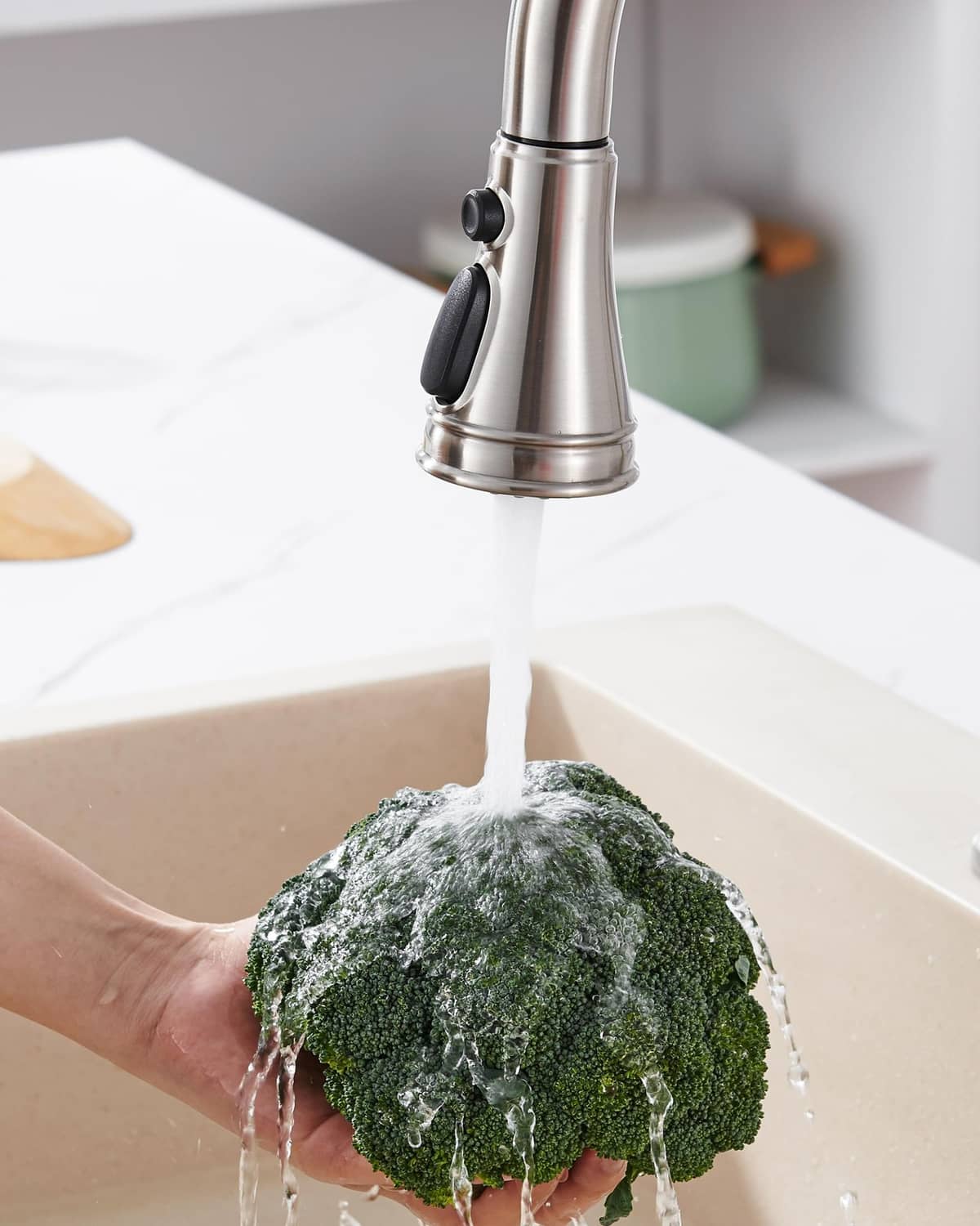 Kitchen faucet spray head pouring water onto green scrub sponge