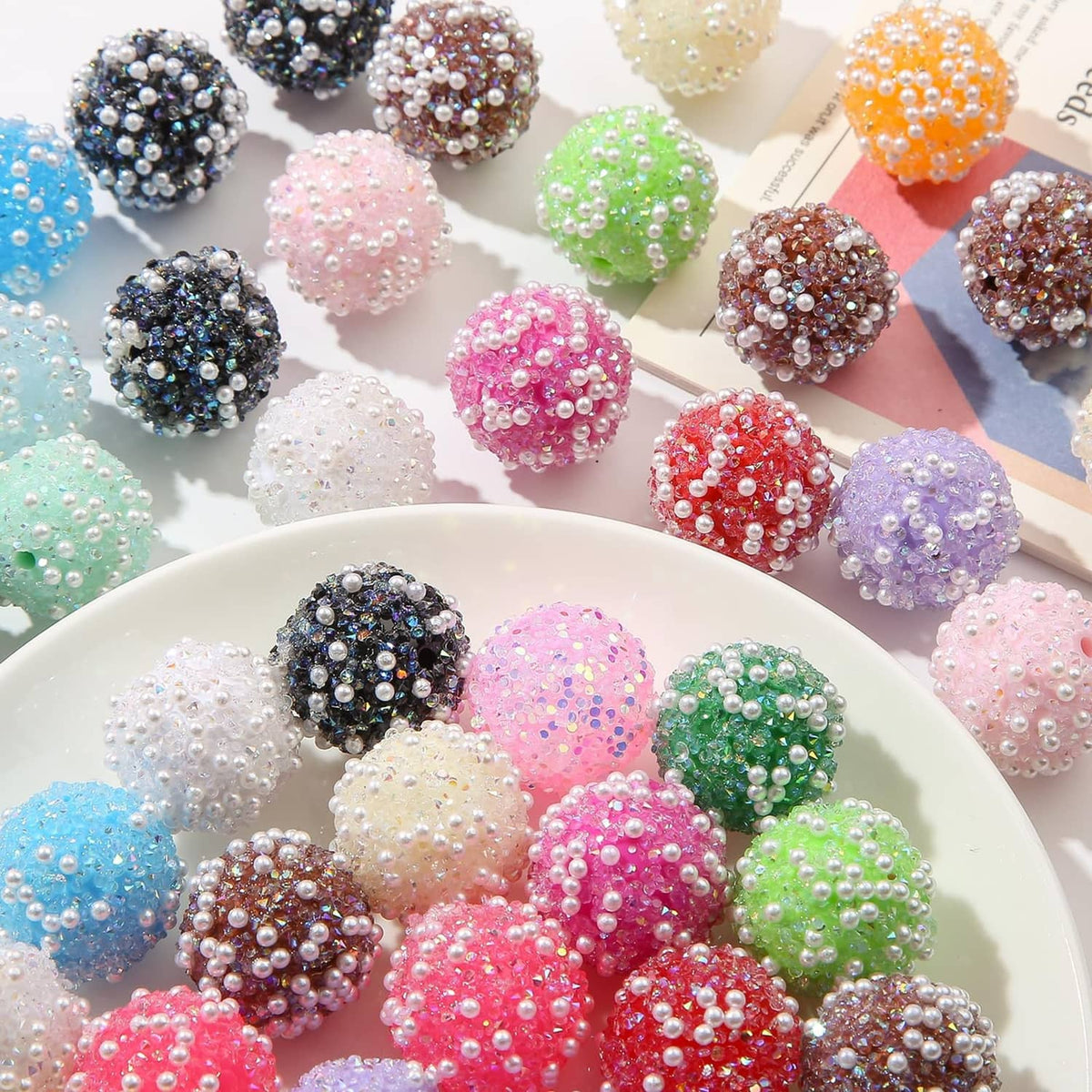 Round acrylic rhinestone beads in assorted colors, some dark and bright pink on tray