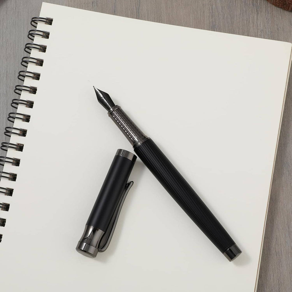Black fountain pen with fine nib and cap beside a spiral notebook