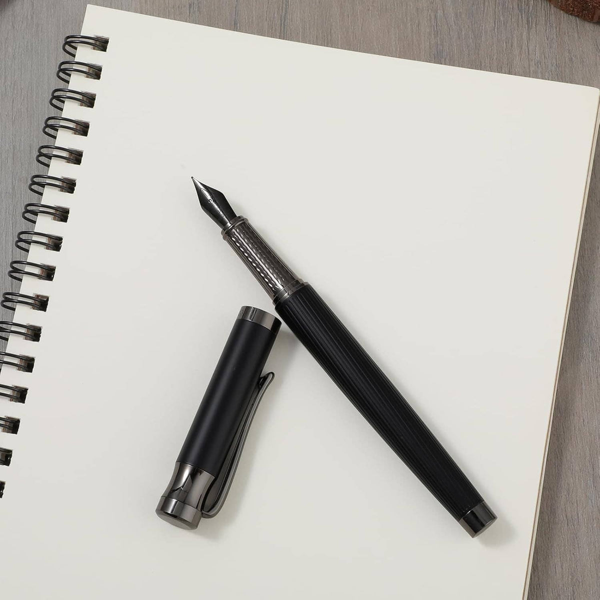 Black fountain pen with fine nib and cap beside a spiral notebook