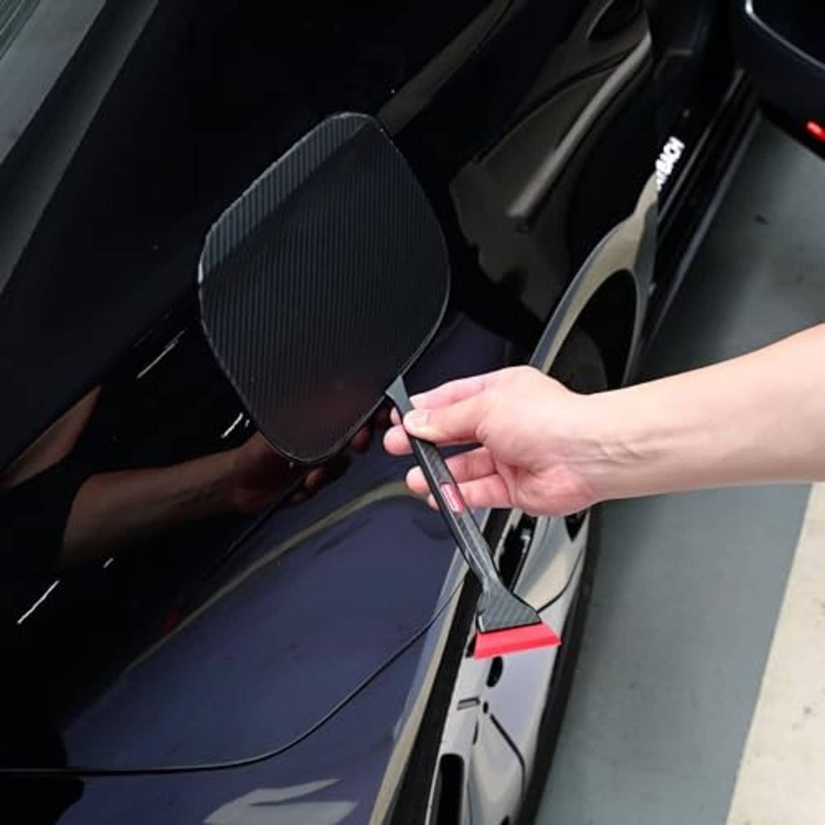 Quarter squeegee tucking window tint tool used along a car door edge, black and red