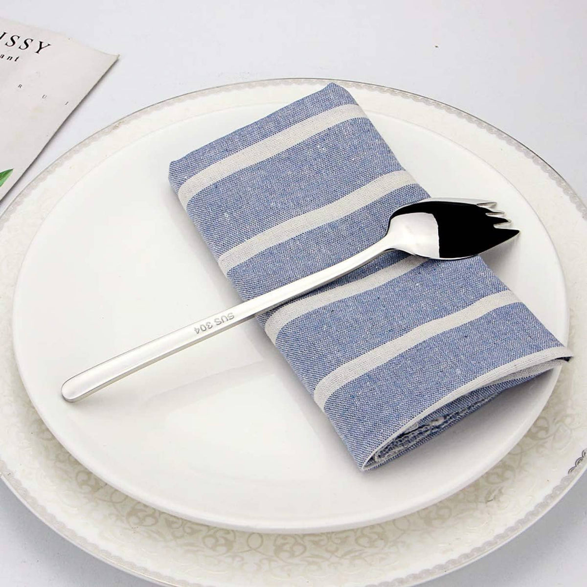 Stainless steel spork resting on blue striped napkin, spoon bowl with tines