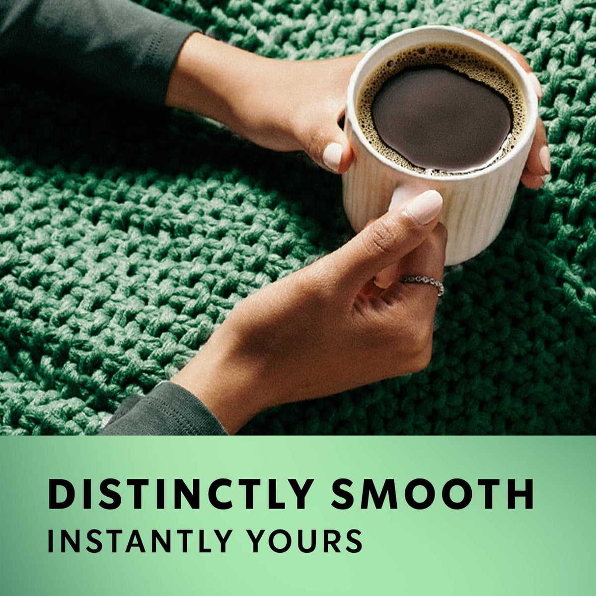 Mug of dark roast instant coffee being held over a textured green fabric surface.