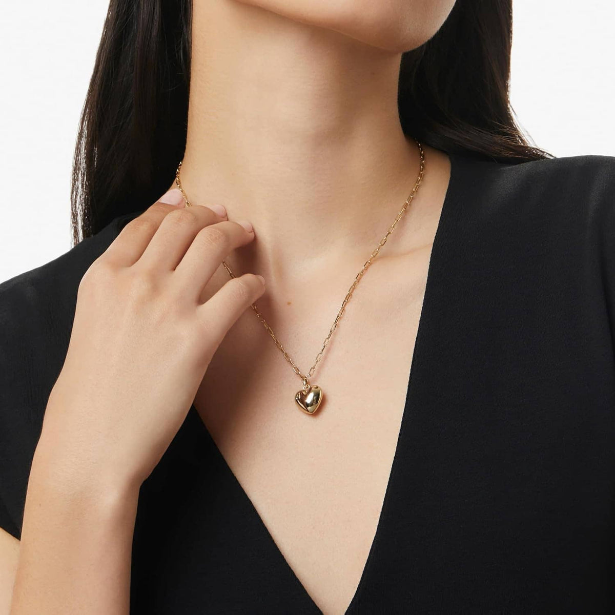 Gold heart pendant necklace on neckline with paperclip-style chain, close-up view