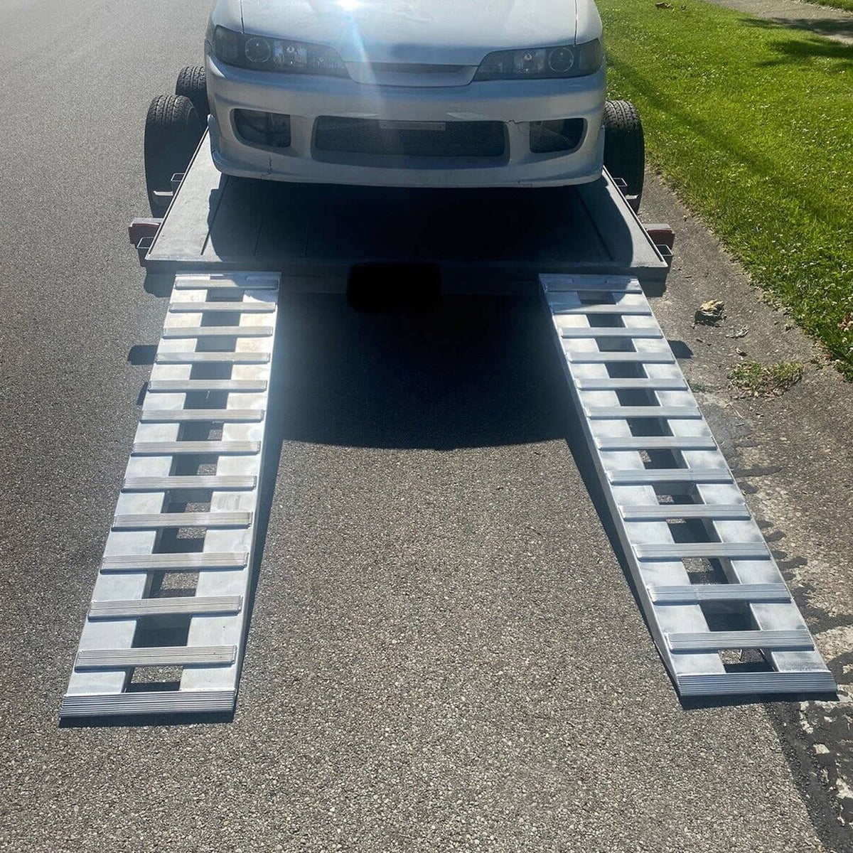 Two aluminum vehicle ramps on asphalt with truck positioned on top