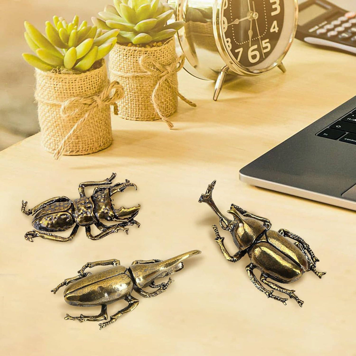 Three brass beetle figurine ornaments placed on a desk surface