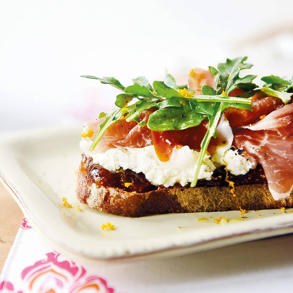 Toast with orange fig spread, topped with prosciutto, basil, and arugula garnish