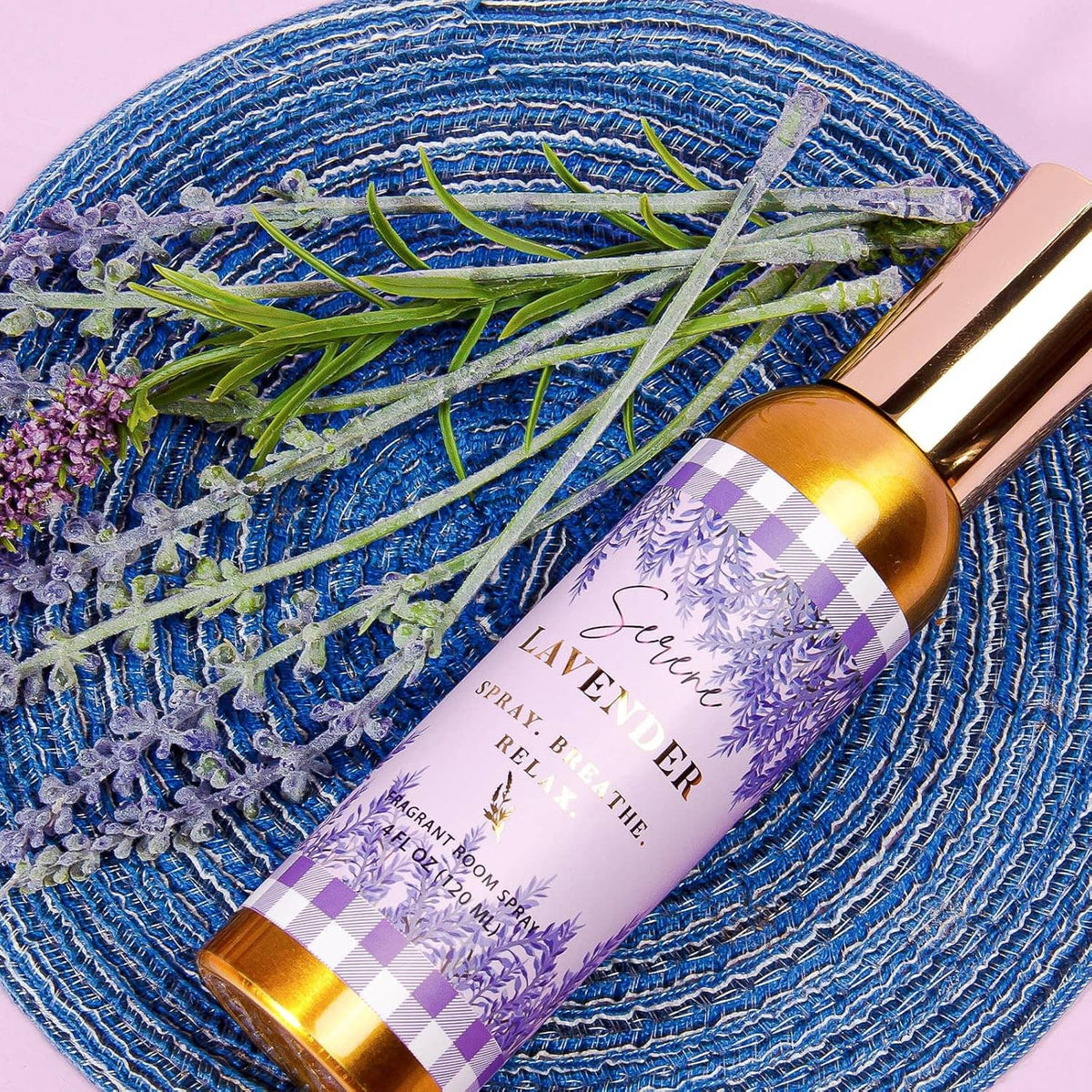Lavender room spray bottle with gold cap resting on blue textured cloth with lavender sprigs