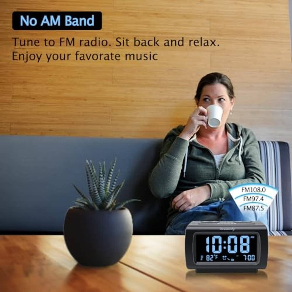Black alarm clock radio on table beside a seated person drinking from a mug