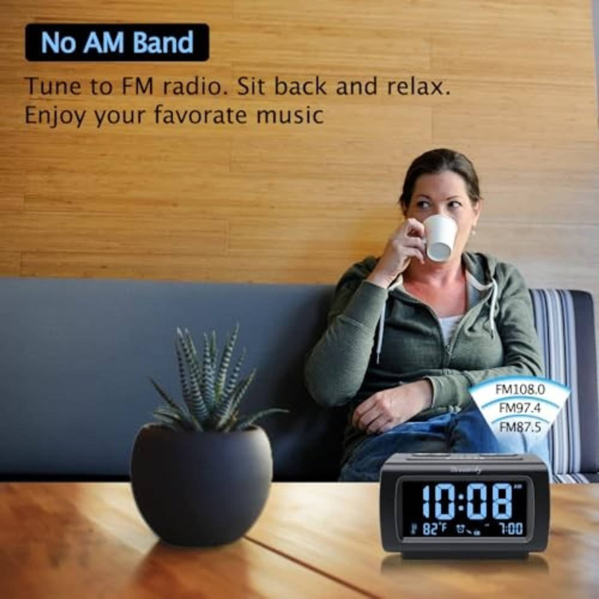 Black alarm clock radio on table beside a seated person drinking from a mug