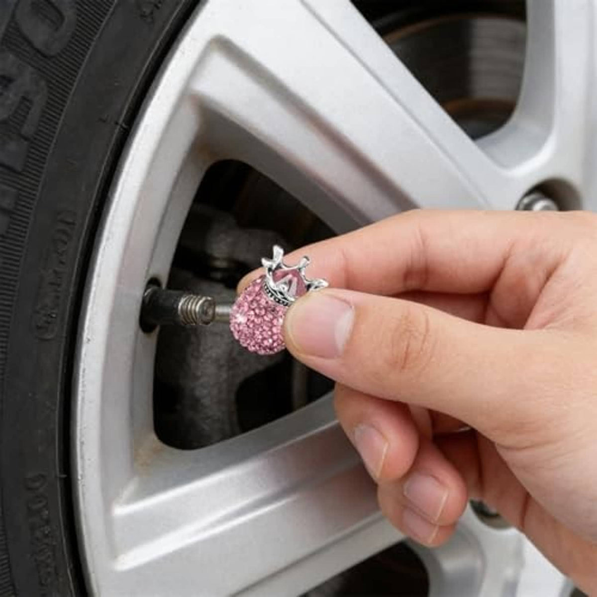 Hand holding a pink rhinestone crown valve stem cap with silver crown detail