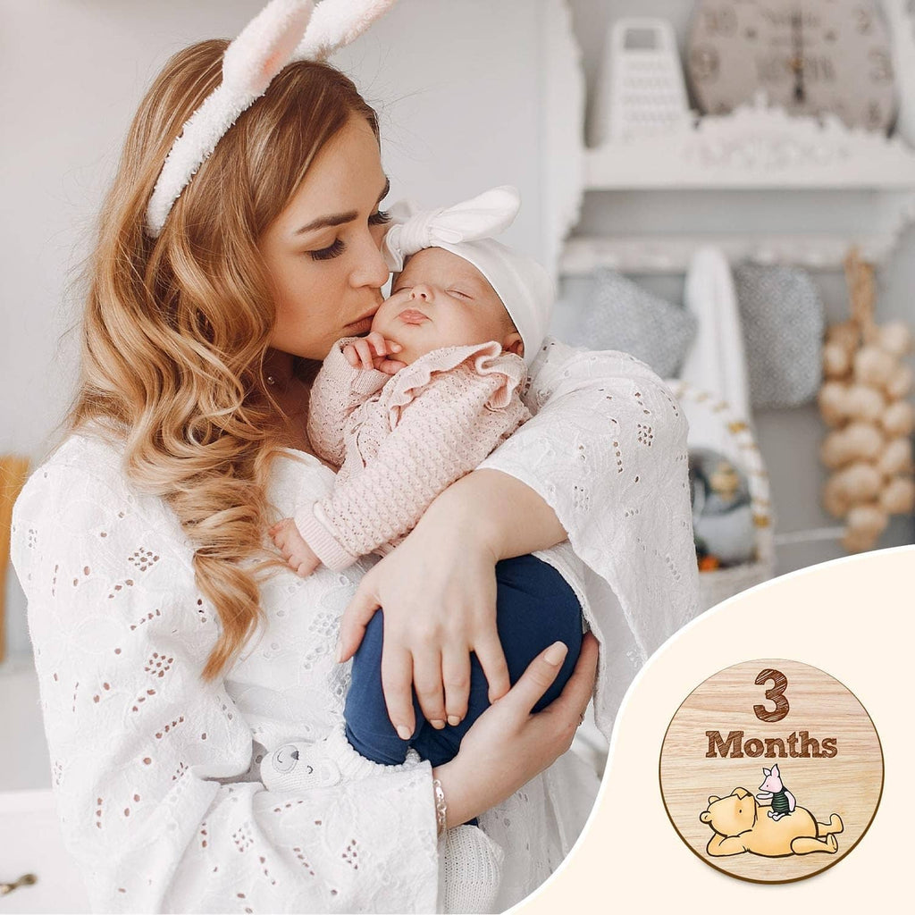 Mother holding newborn, with a round wooden milestone sign showing 3 months.