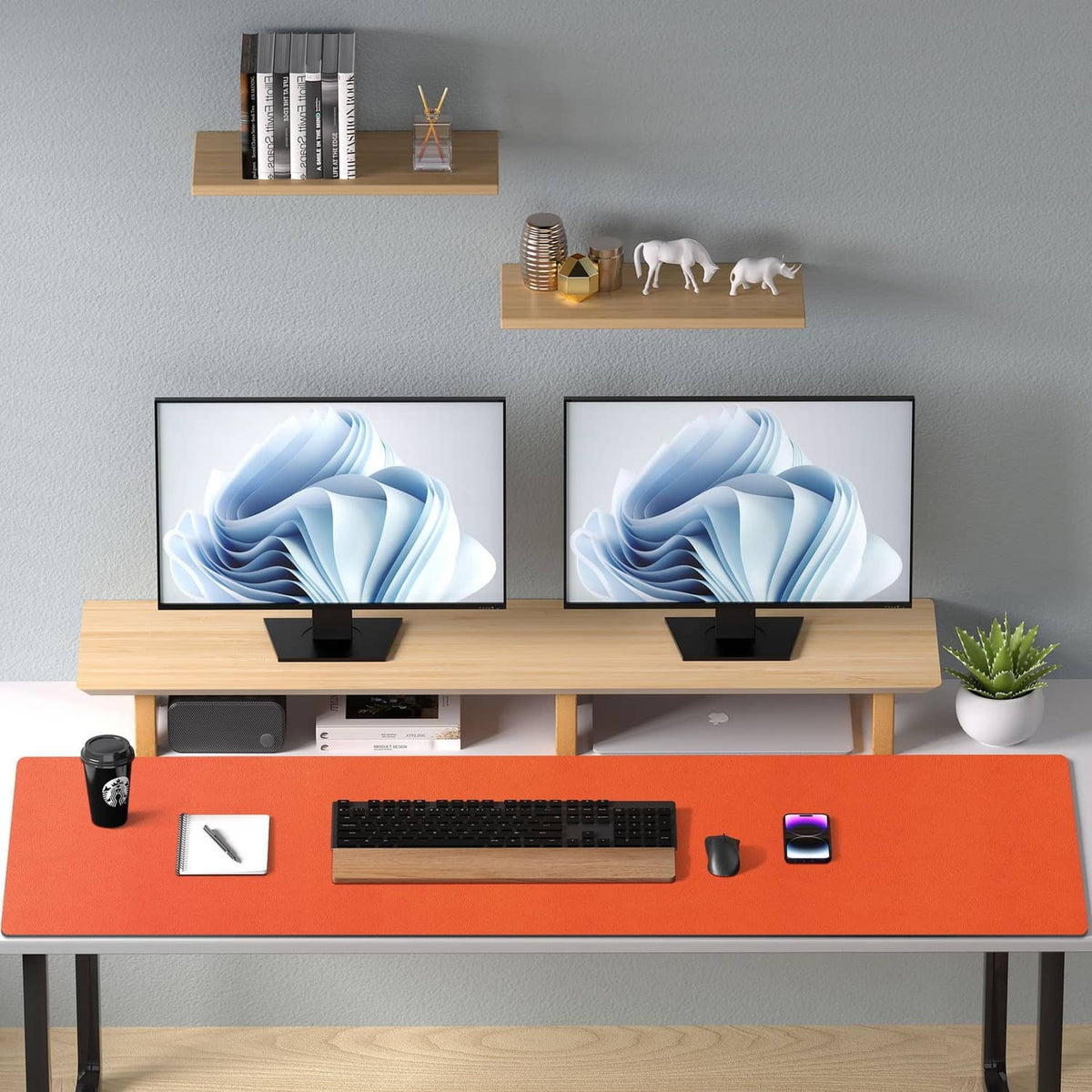 Orange desk pad protector on tabletop beneath dual monitors and office items