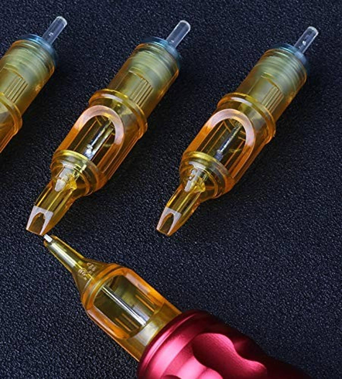 Three orange disposable tattoo needles on dark textured surface